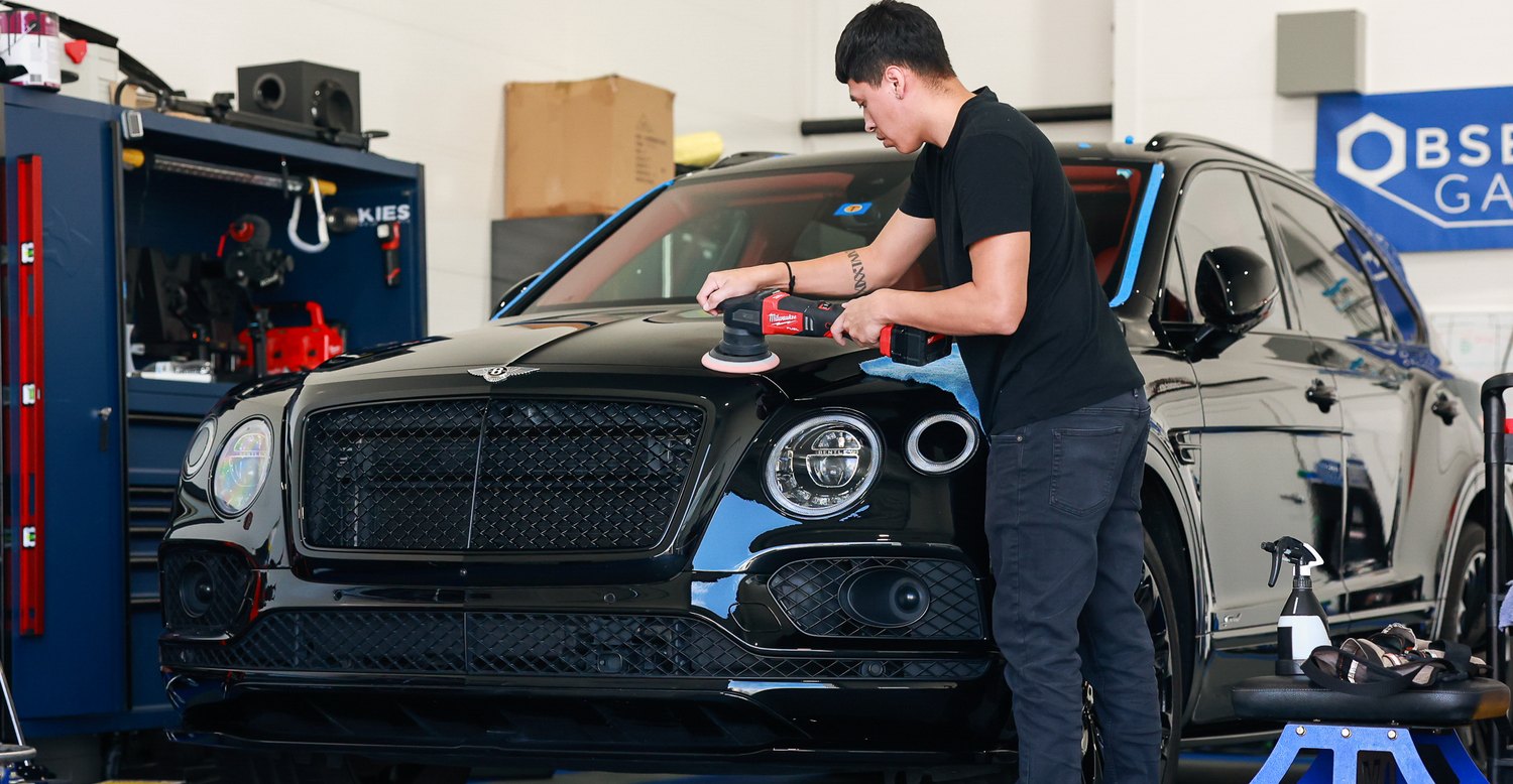 Polishing the hood of a black Bentley Bentayga Speed in the shop