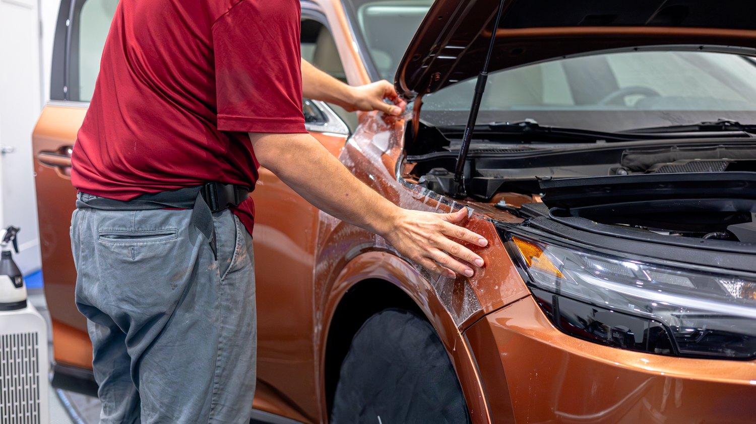 Installing PPF on the front fender of a copper Lexus RX 350 with the hood open