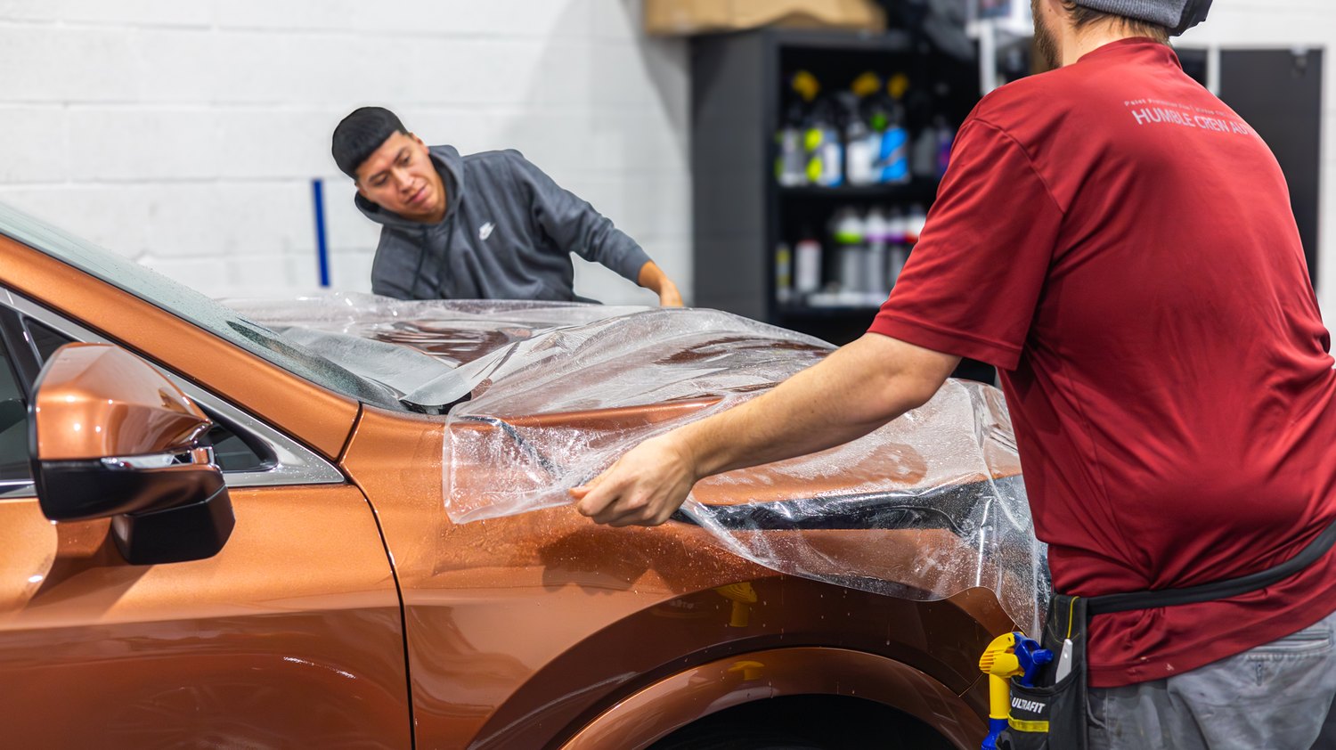 Two installers laying PPF on the hood of a copper Lexus RX 350