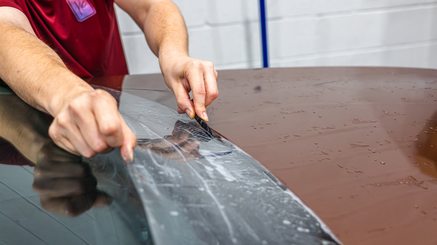 Hand trimming PPF along the windshield edge of a Lexus RX 350 hood