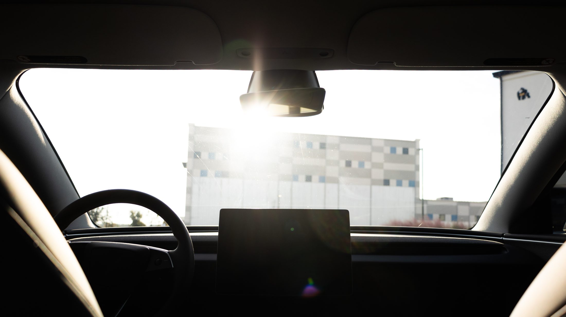 The view out of a windshield with no ceramic tint — the sky is blown out with glare